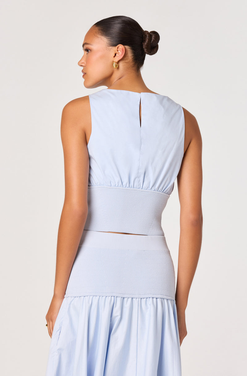Woman wearing a sleeveless light blue top with a high waistband and a matching skirt.