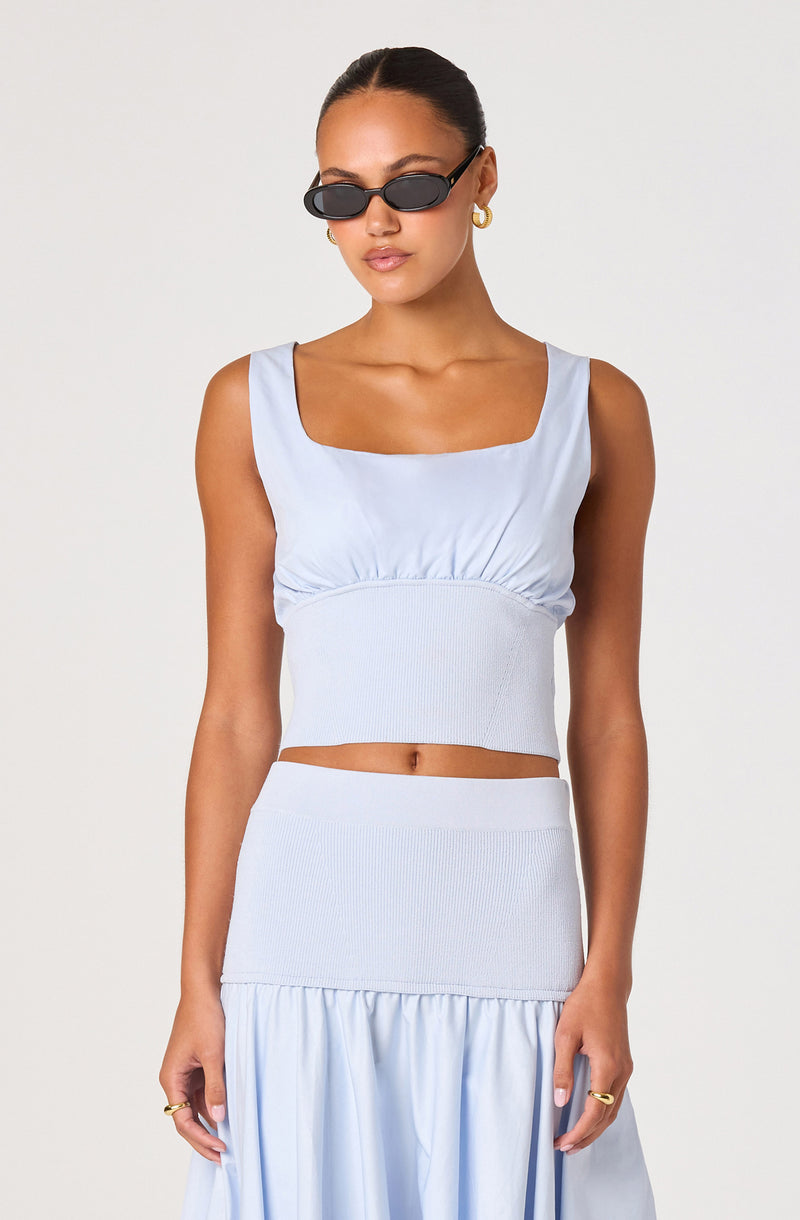 Woman wearing a light blue sleeveless crop top with a square neckline and a matching high-waisted skirt.