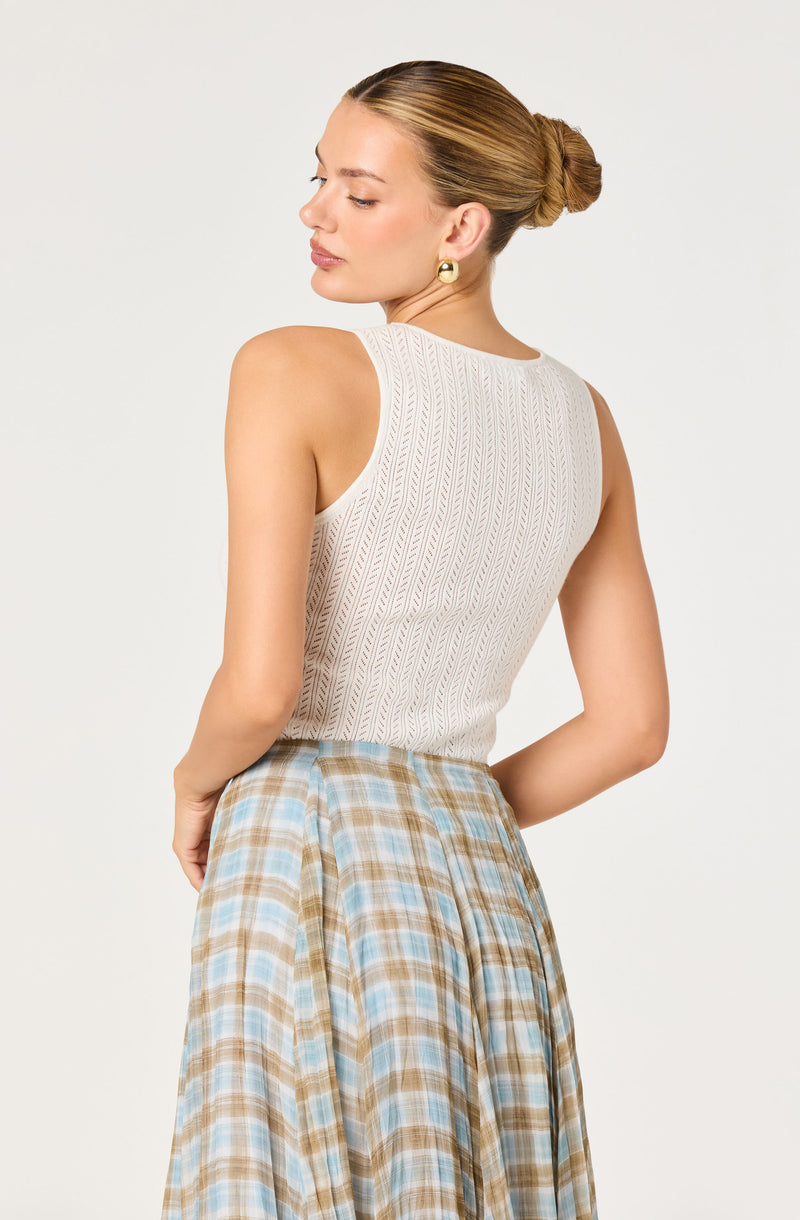 Woman wearing a cream sleeveless top with a textured pattern and a blue-checked skirt.