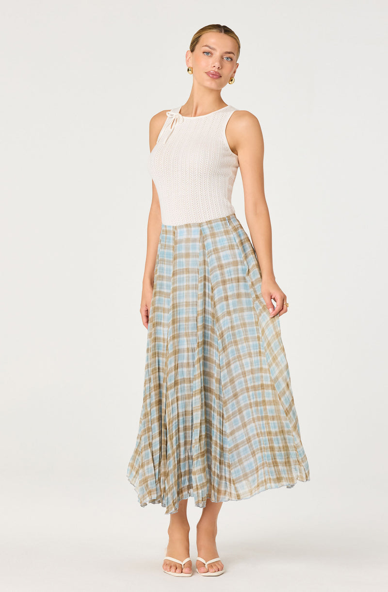 Woman wearing a white sleeveless knit top with ruffled shoulder detail and beige-blue plaid wide-leg skirt.