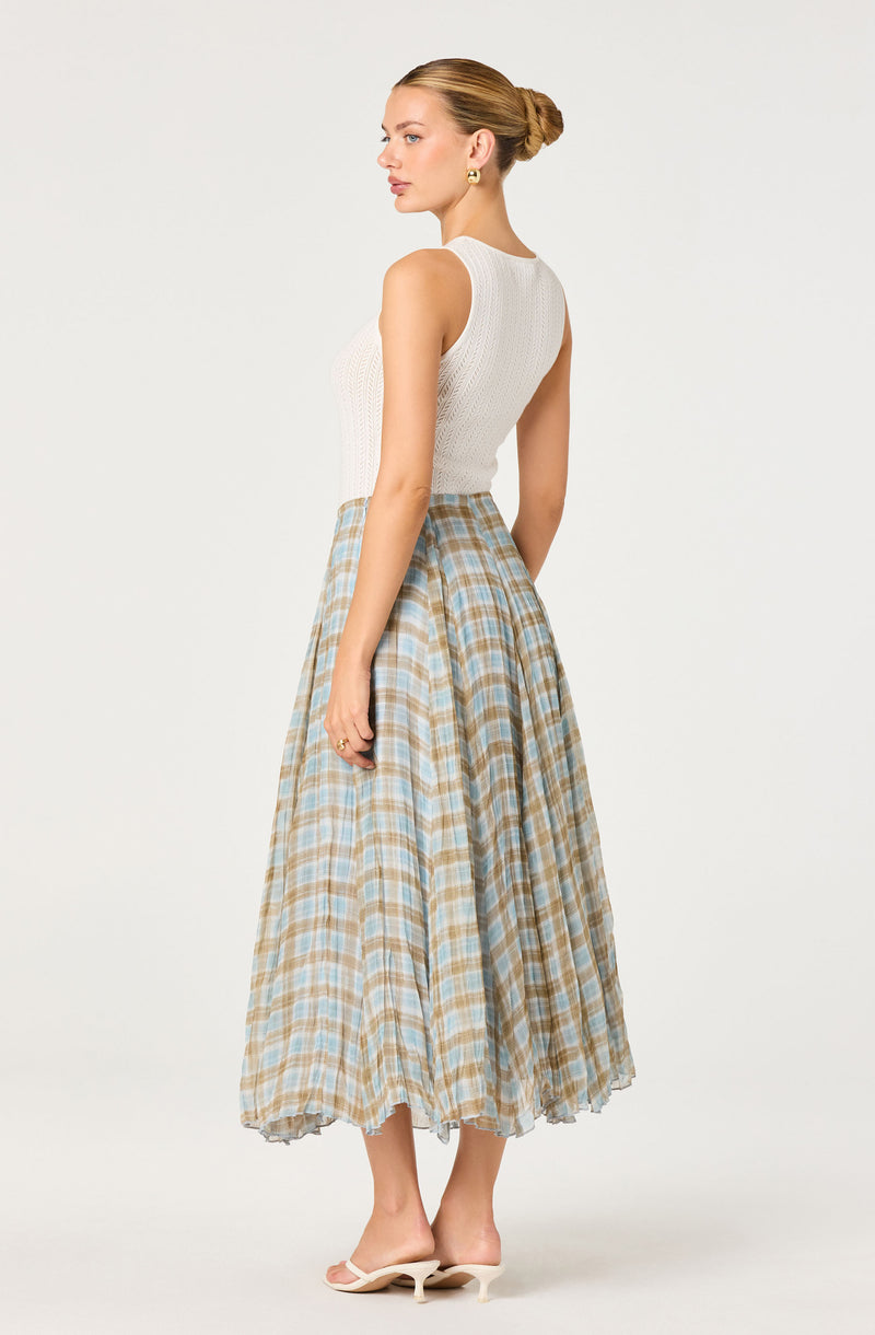 Woman wearing a sleeveless white textured top and a high-waisted, plaid beige and blue midi skirt.
