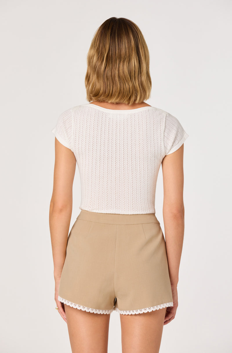 White short-sleeve top with a textured pattern and beige shorts with lace trim at the hem.