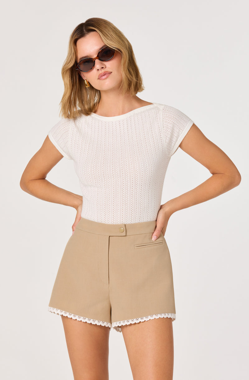 Woman wearing a white textured short-sleeve top and beige shorts with a lace trim.