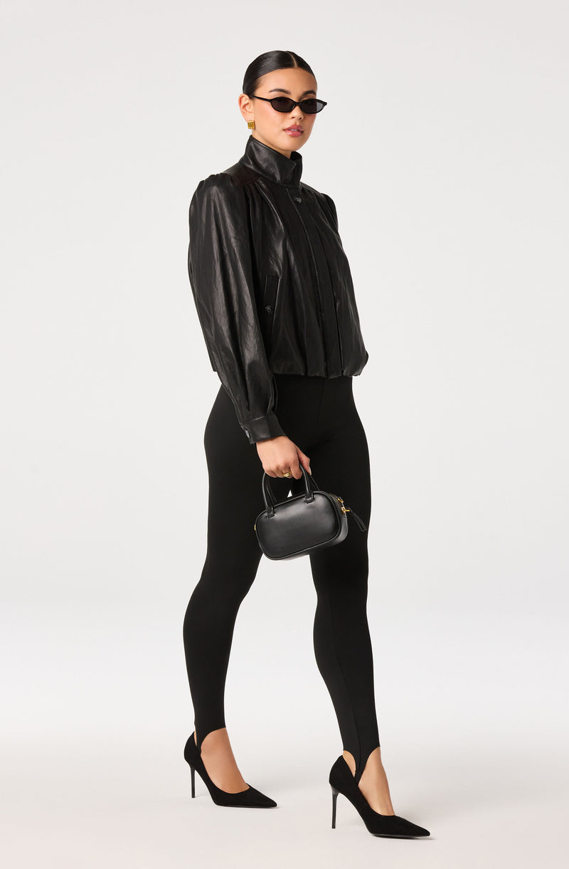 Woman wearing a black leather jacket, black leggings, black high heels, and sunglasses, holding a small black handbag.