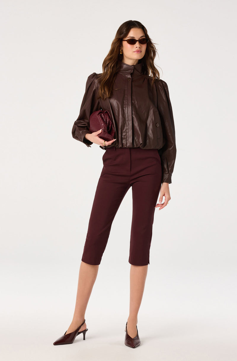Woman in dark brown leather jacket, maroon cropped pants, pointed heels, and sunglasses, holding a maroon clutch.