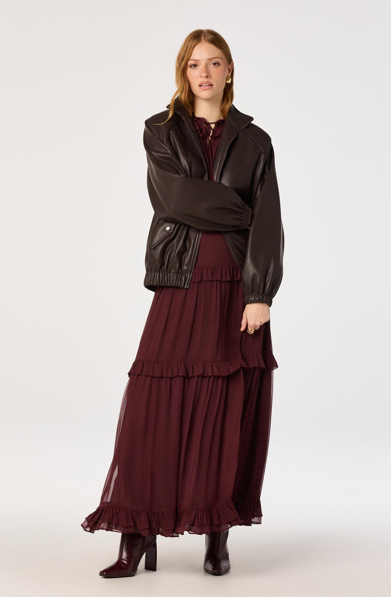 Girl wearing a black leather jacket over a burgundy ruffled dress with matching burgundy boots.