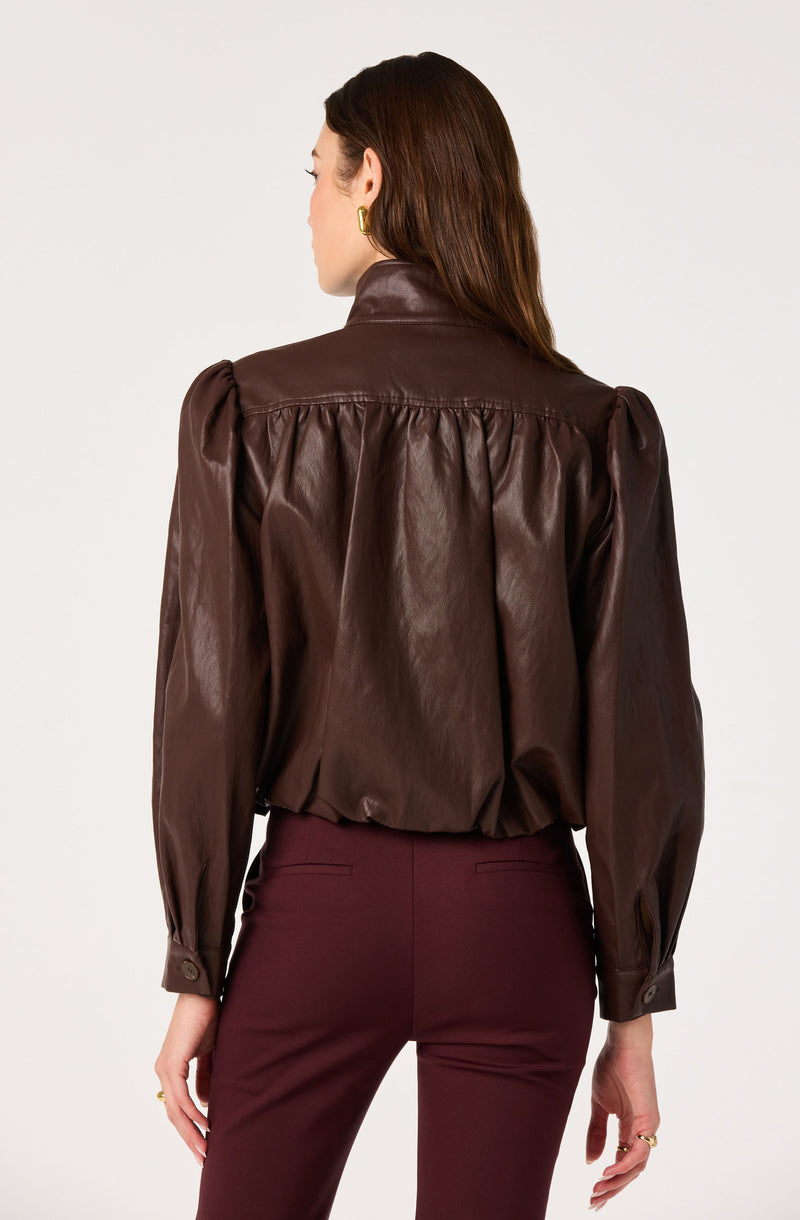 Woman wearing a brown leather jacket with puffed sleeves and high-waisted burgundy pants.