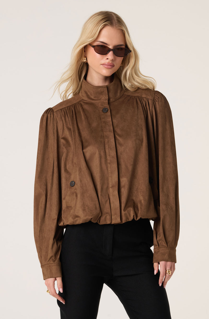 Woman wearing a brown suede button-up shirt with puffed long sleeves, paired with black pants.