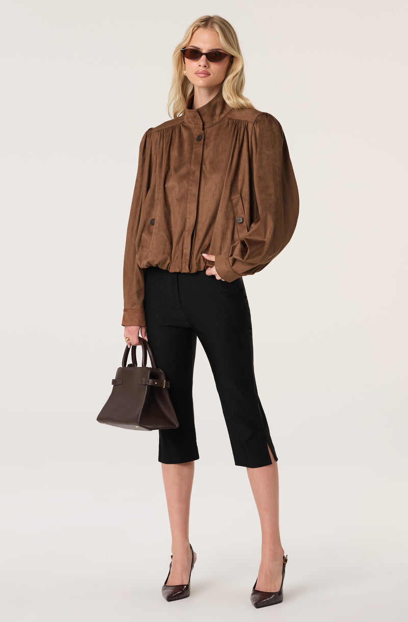Woman wearing a brown oversized suede jacket with puffed sleeves, black cropped pants, and high heels.