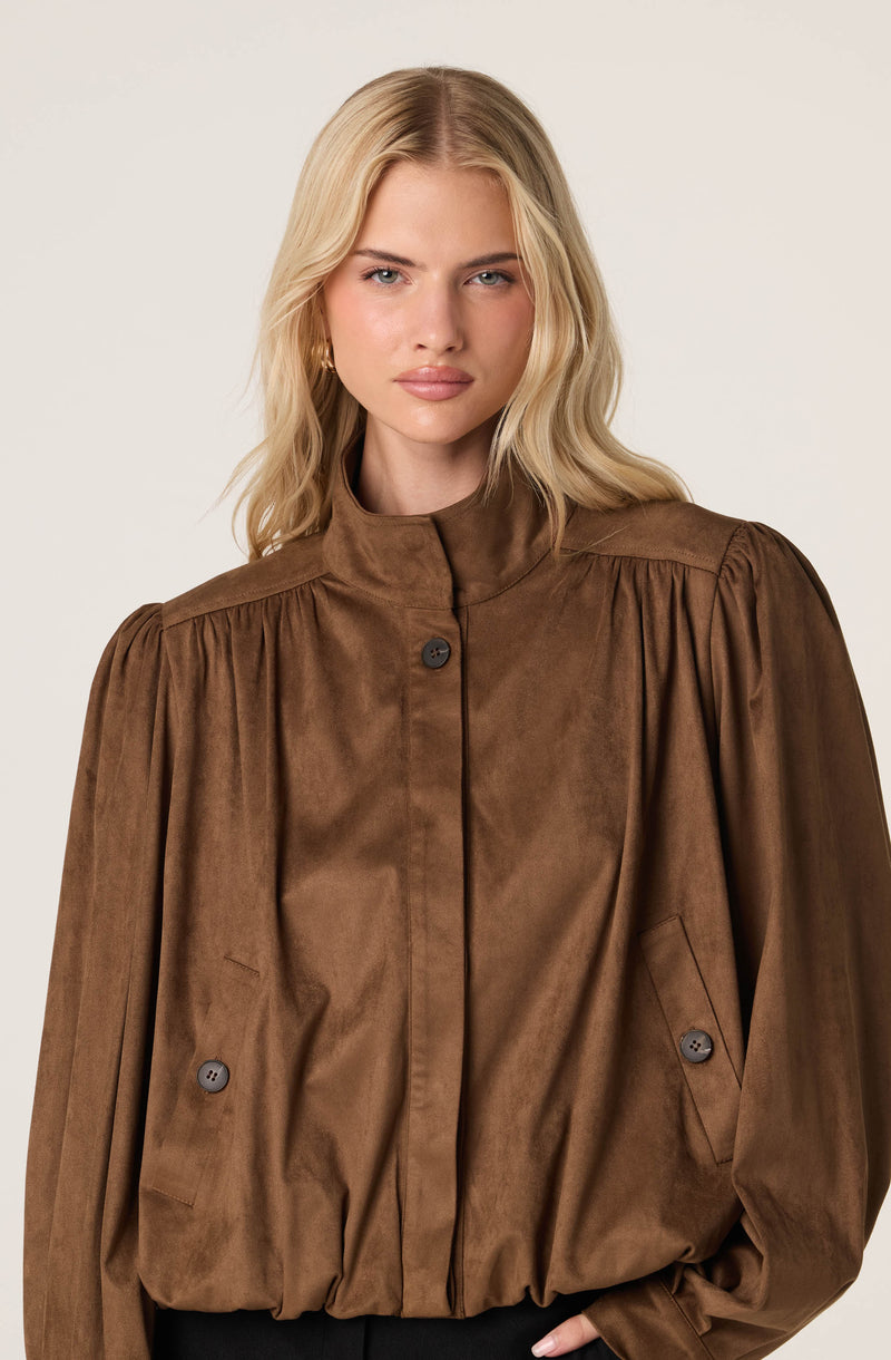 Woman wearing a brown, loose-fitting, button-up jacket with gathered fabric and shoulder pleats.
