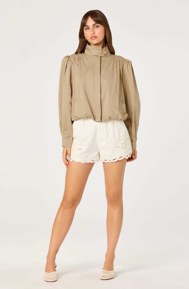 Woman wearing a beige blouse with puffed sleeves and white shorts with scalloped edges.