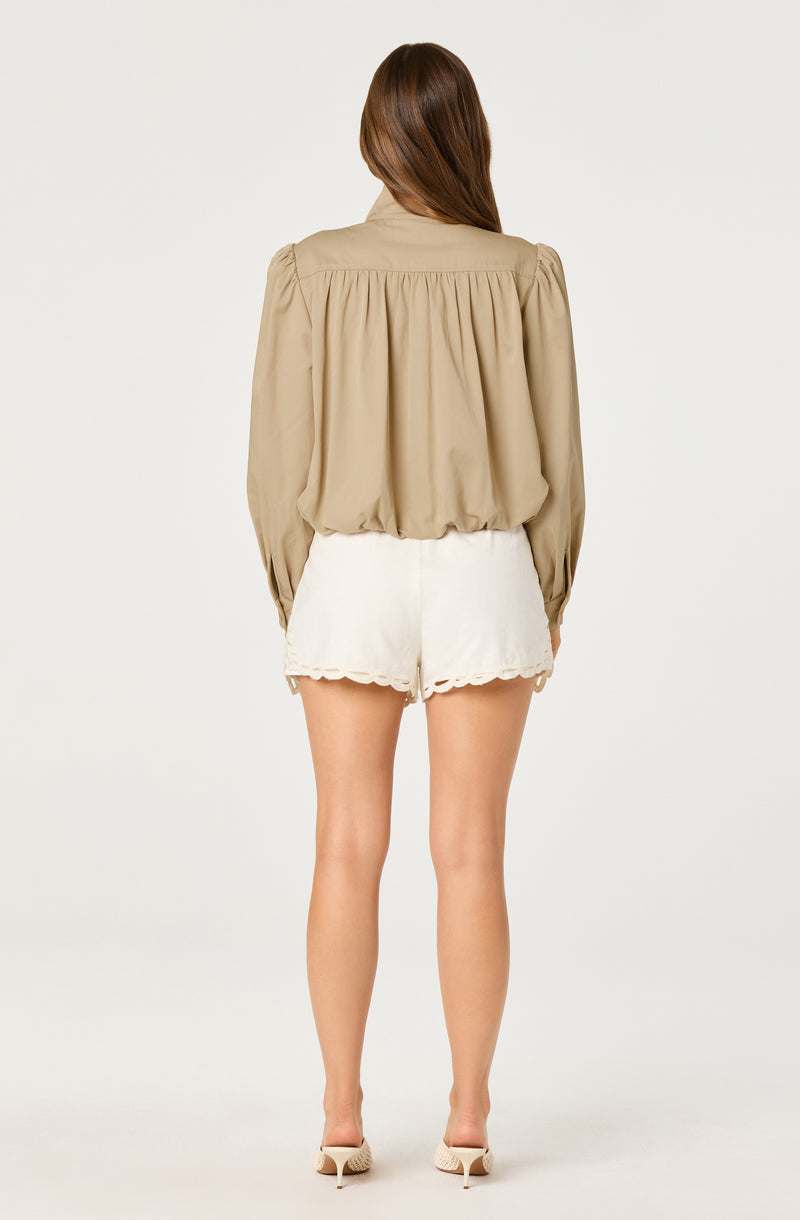 Woman wearing a beige long-sleeve blouse and white lace-trimmed shorts.