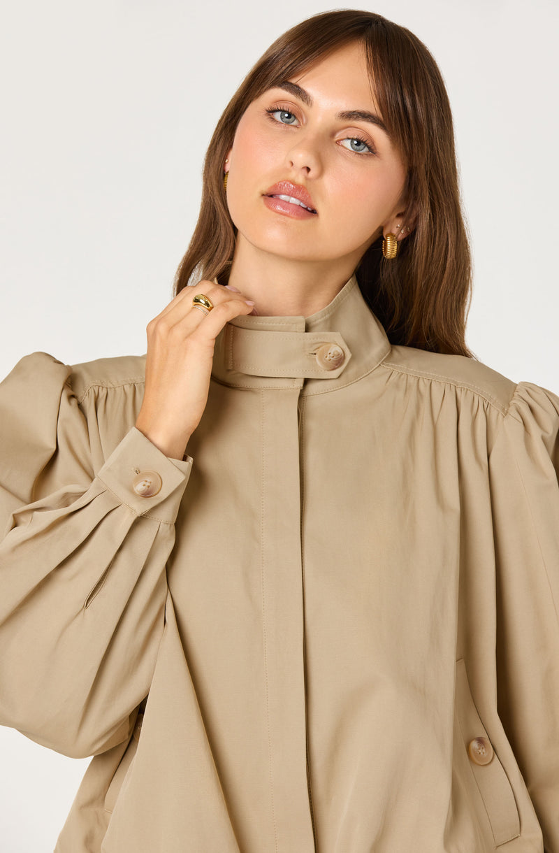 Woman in beige high-neck, puff-sleeve blouse with large buttons.