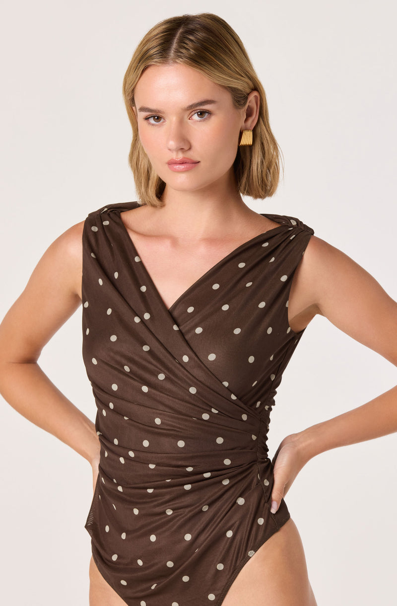 Woman in brown polka dot one-piece swimsuit with pleats and a draped design.
