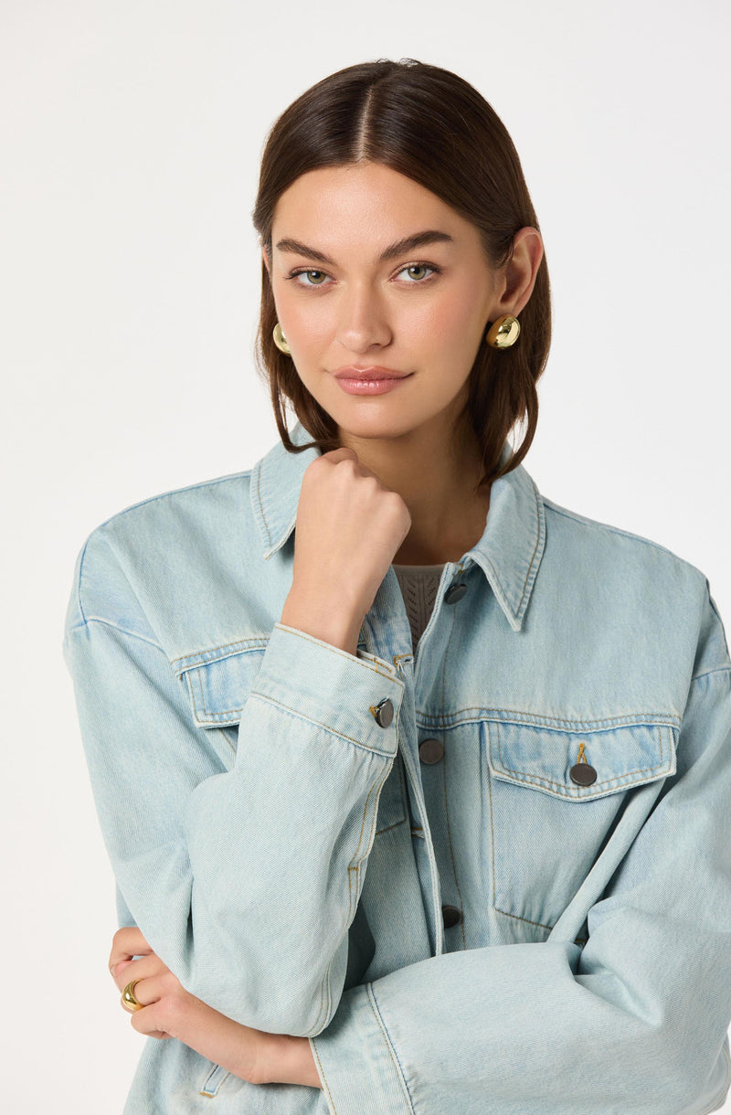 Woman wearing a light blue denim jacket and large gold earrings.