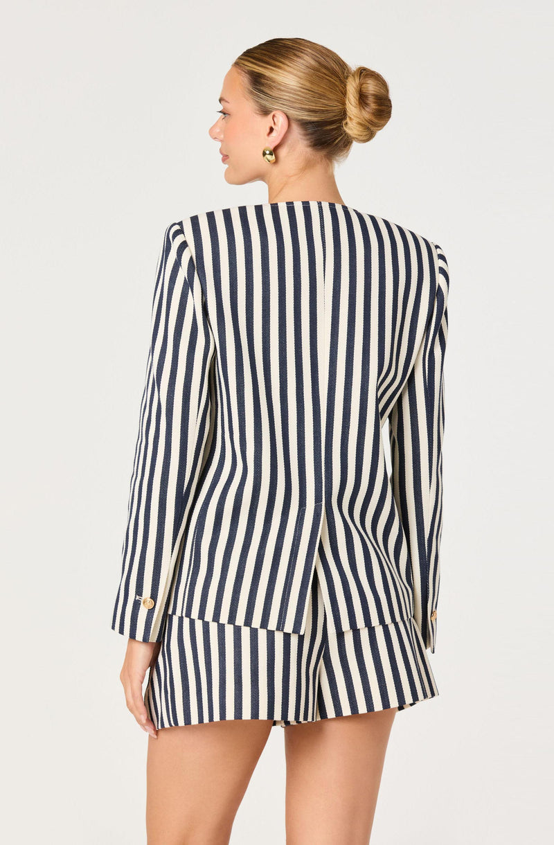 Woman wearing a navy and white vertically striped blazer and matching shorts, with her hair in a bun.