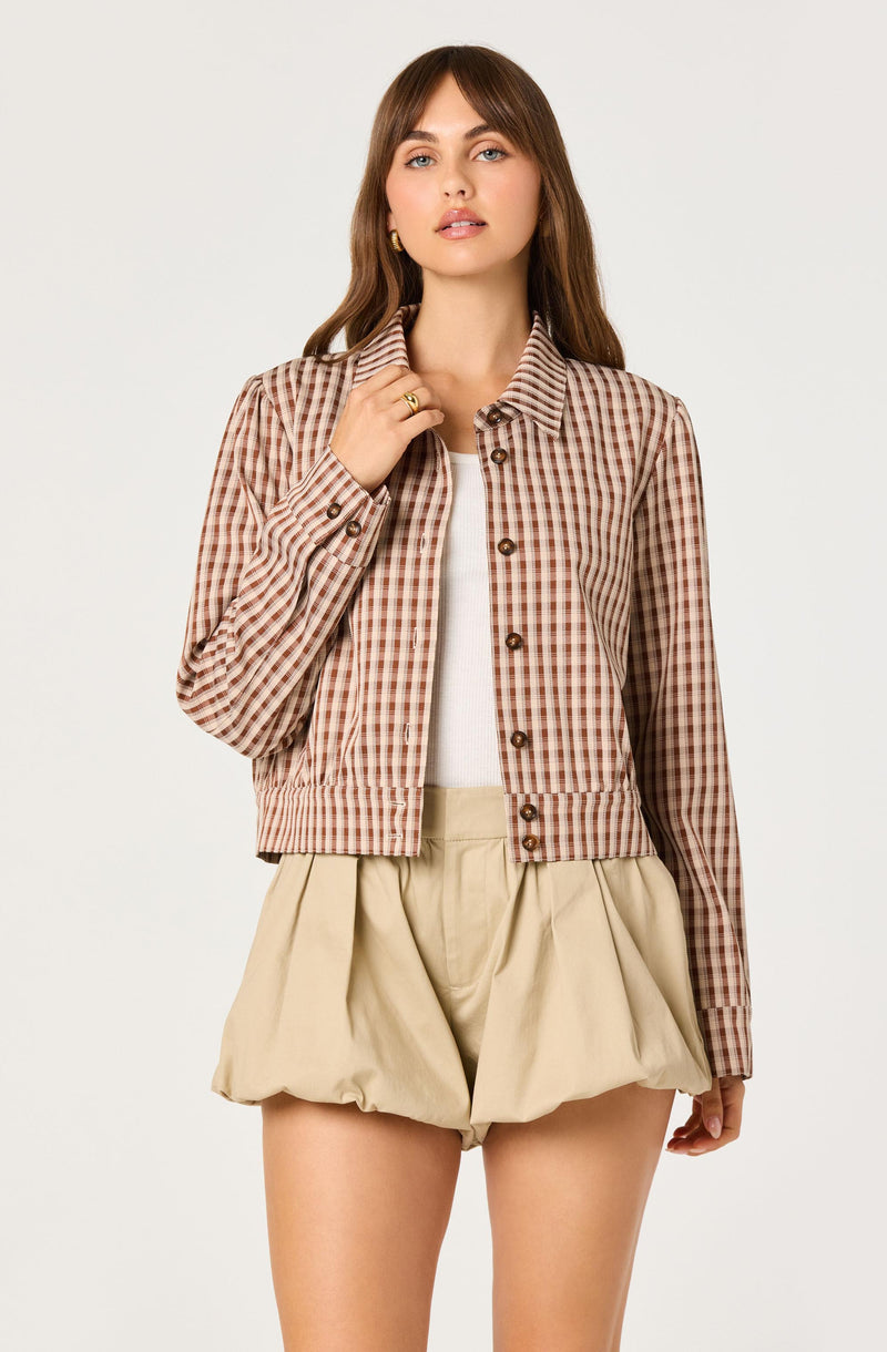 Woman wearing a brown checkered jacket with brown buttons, beige shorts, and a white top.