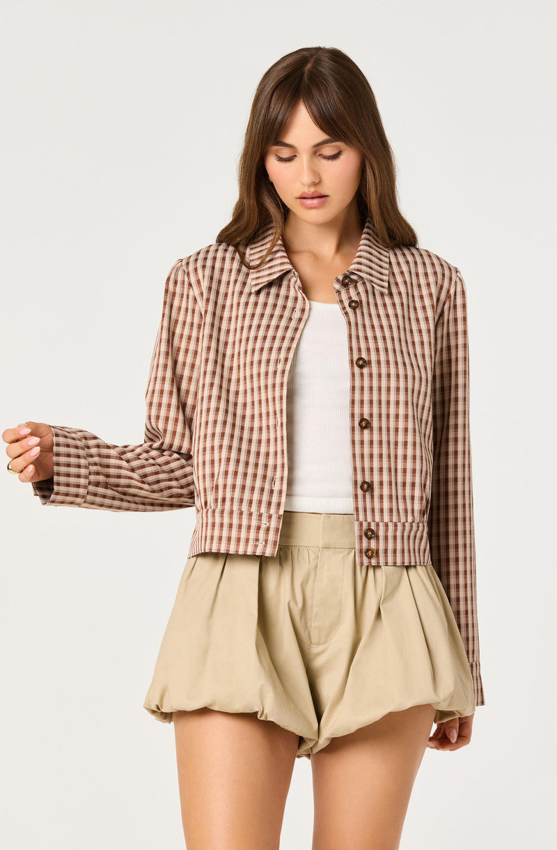 Woman wearing a beige checkered jacket over a white top and beige puffed shorts.