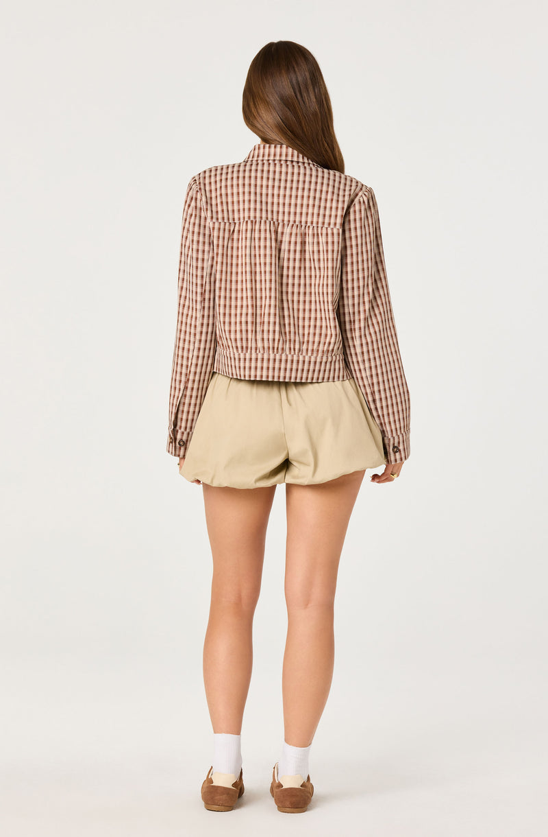 Woman wears a long-sleeve gingham shirt and beige shorts.