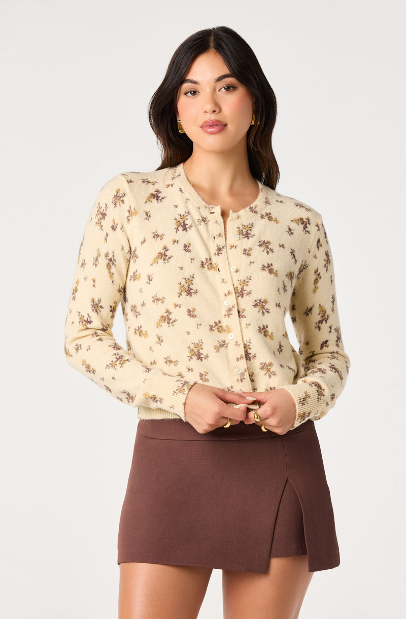 Woman wearing a cream cardigan with small floral patterns and a brown skirt with a front slit.
