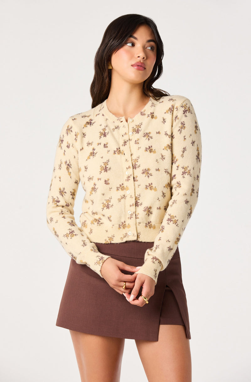 Woman wearing a cream sweater with floral pattern and brown skirt.