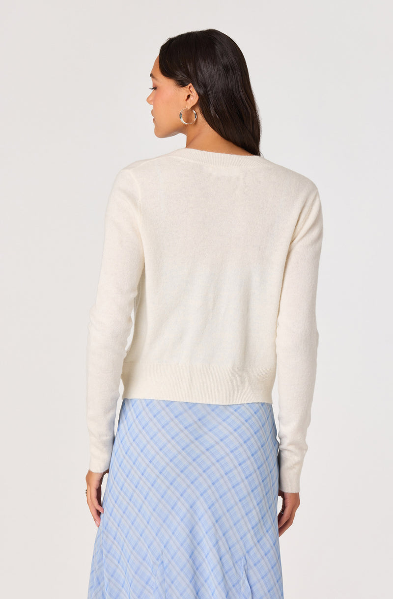 Woman in cream sweater and blue plaid skirt, facing away.