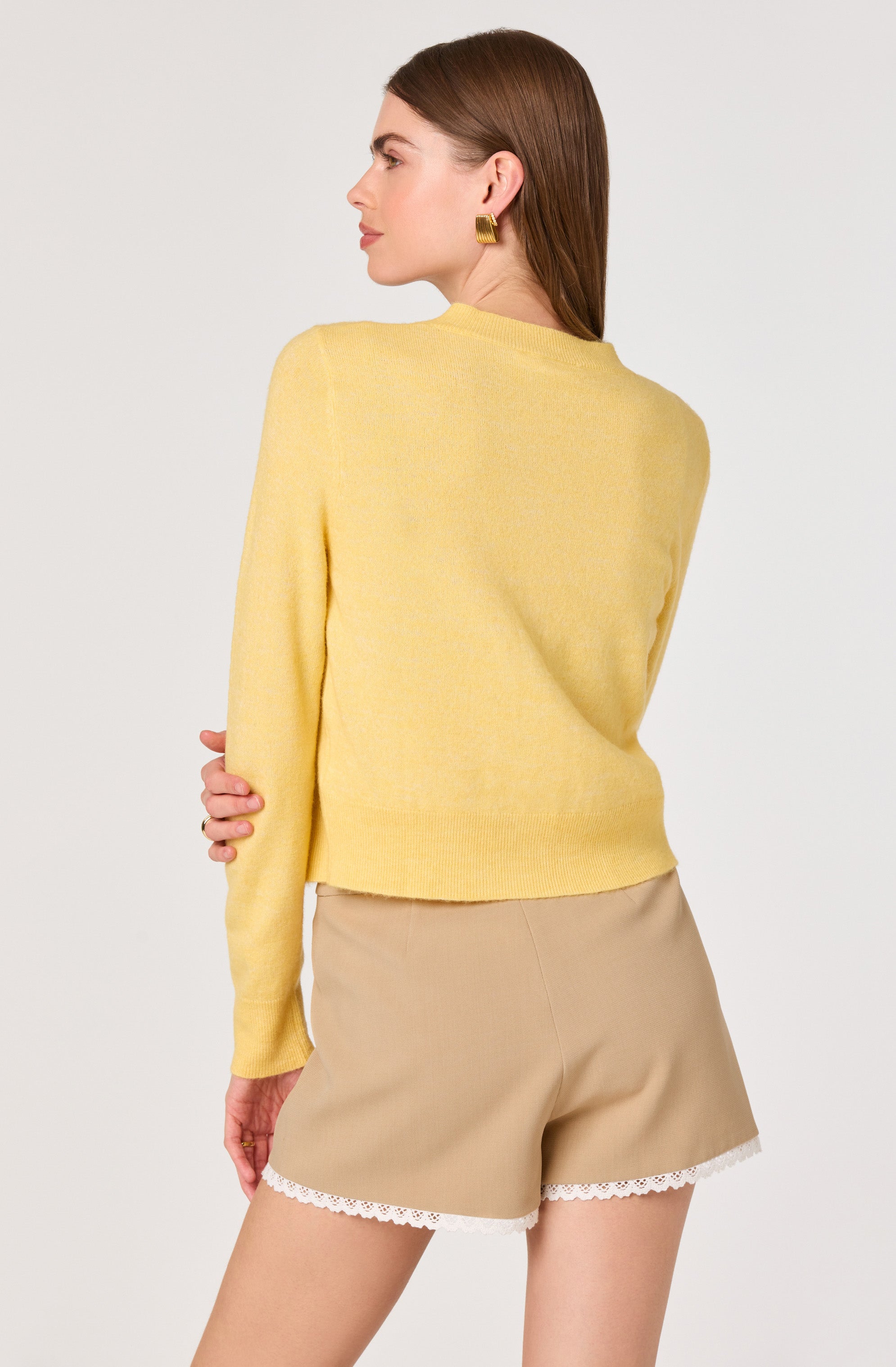 Woman in a yellow long-sleeve sweater and beige shorts with white lace trim.