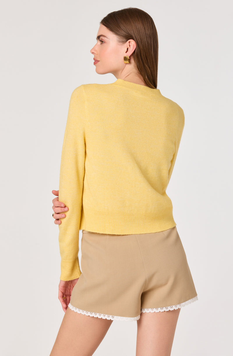 Woman in a yellow long-sleeve sweater and beige shorts with white lace trim.