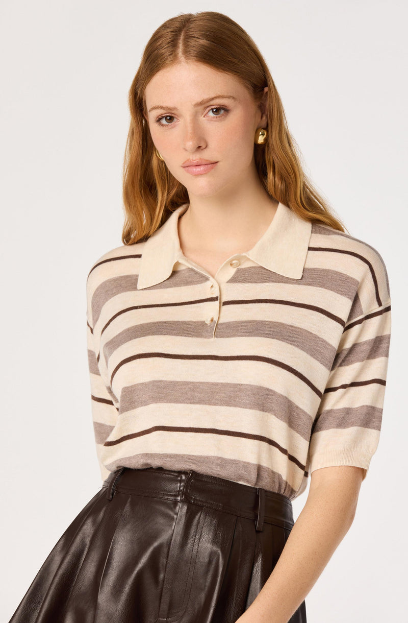 Woman wearing a beige and brown striped collared shirt with short sleeves, tucked into a high-waisted black leather skirt.