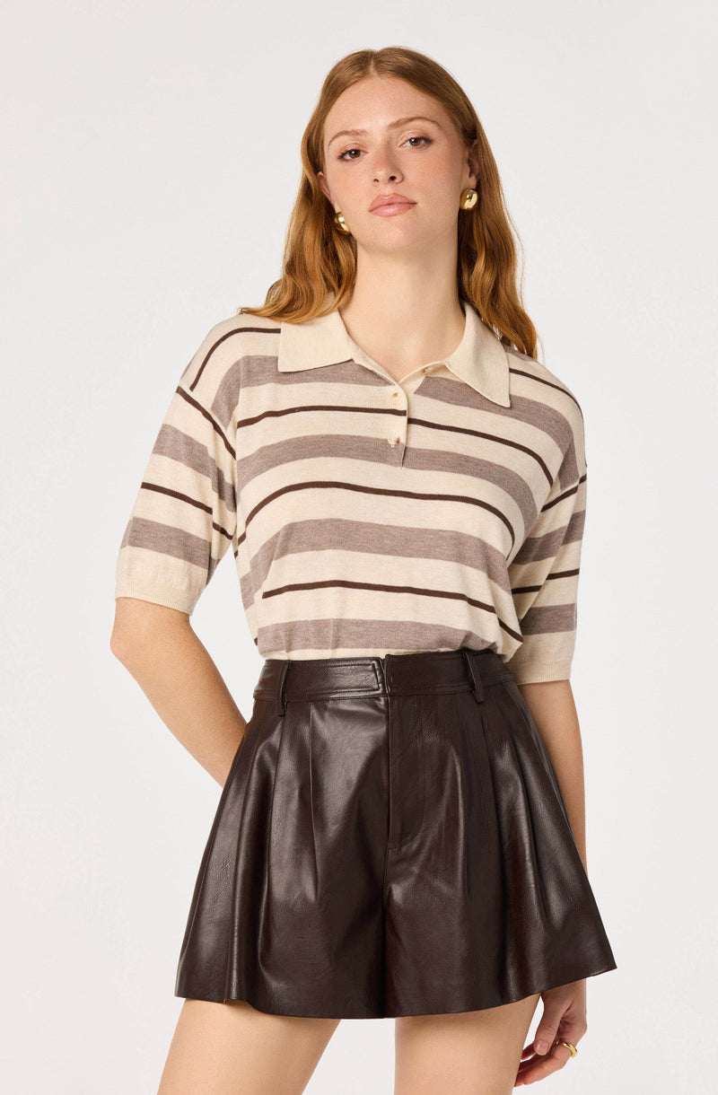 Woman wearing a beige and brown striped polo shirt with short sleeves, paired with high-waisted dark brown leather shorts.