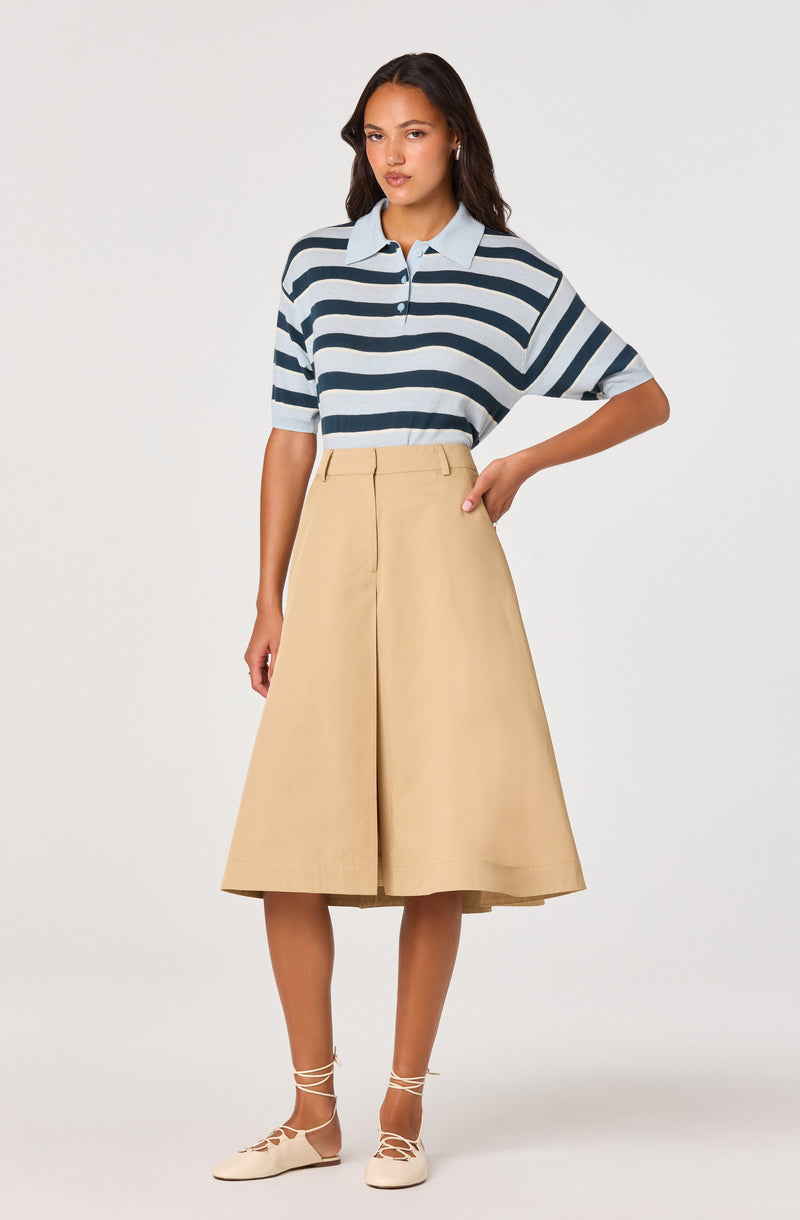 Woman wearing a blue and white striped polo shirt, beige wide-leg skirt, and beige lace-up shoes.