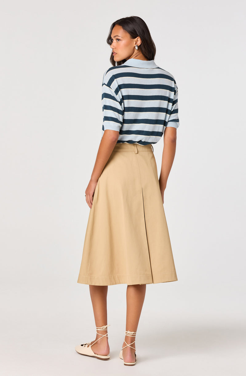 Woman in a blue and white striped top, beige A-line skirt, and beige lace-up flats.