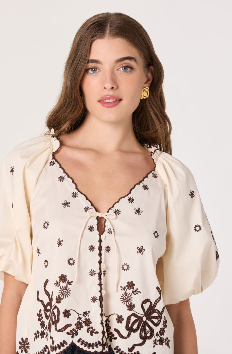 Cream-colored blouse with dark brown floral embroidery and puffed sleeves.