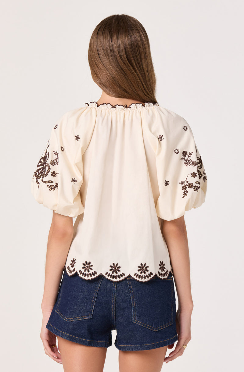 Cream blouse with black floral embroidery and scalloped hem, puffed sleeves.
