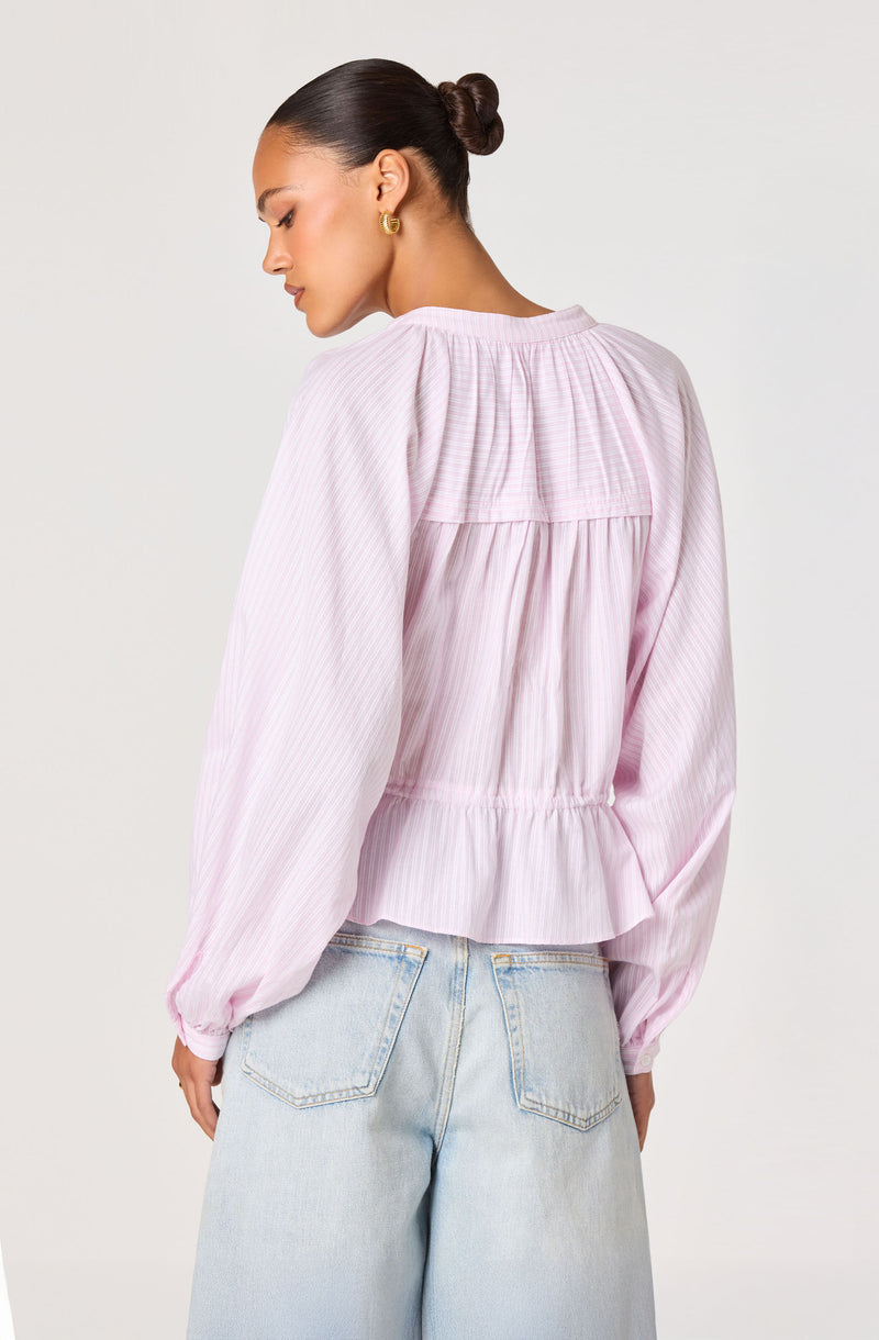 Woman wearing a light pink, long-sleeve, pleated blouse with a ruffled hem.