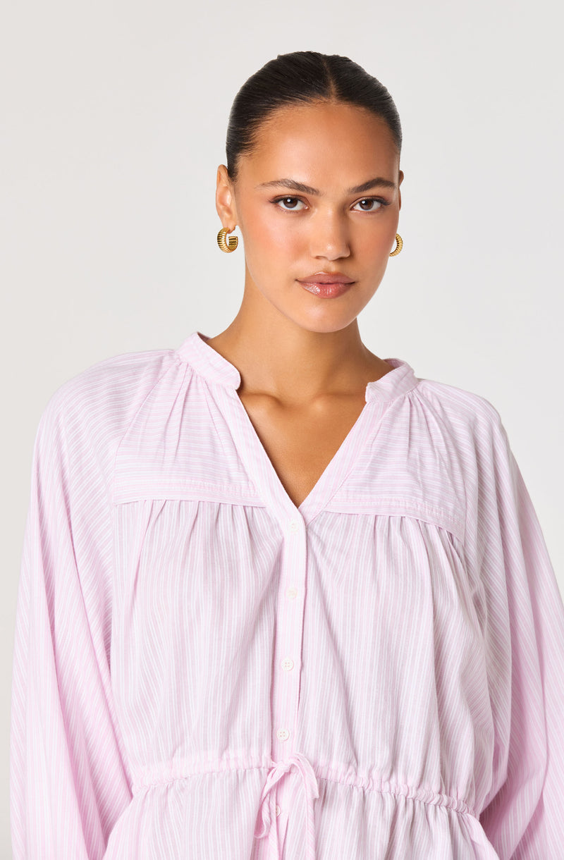 Woman in a light pink, striped, button-up dress with a drawstring waist and puffed sleeves.