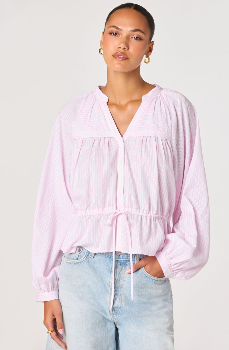 Woman wearing a light pink, long-sleeve, collared blouse with a drawstring waist.
