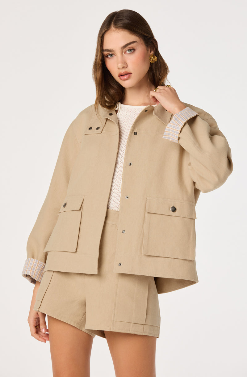 Model wearing a beige jacket with large front pockets and matching beige shorts, with cuffs showing a plaid pattern.