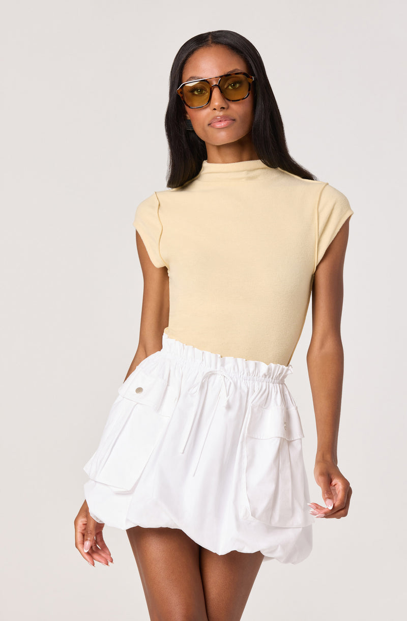 Woman wearing a beige sleeveless top and white gathered cargo-style skirt.