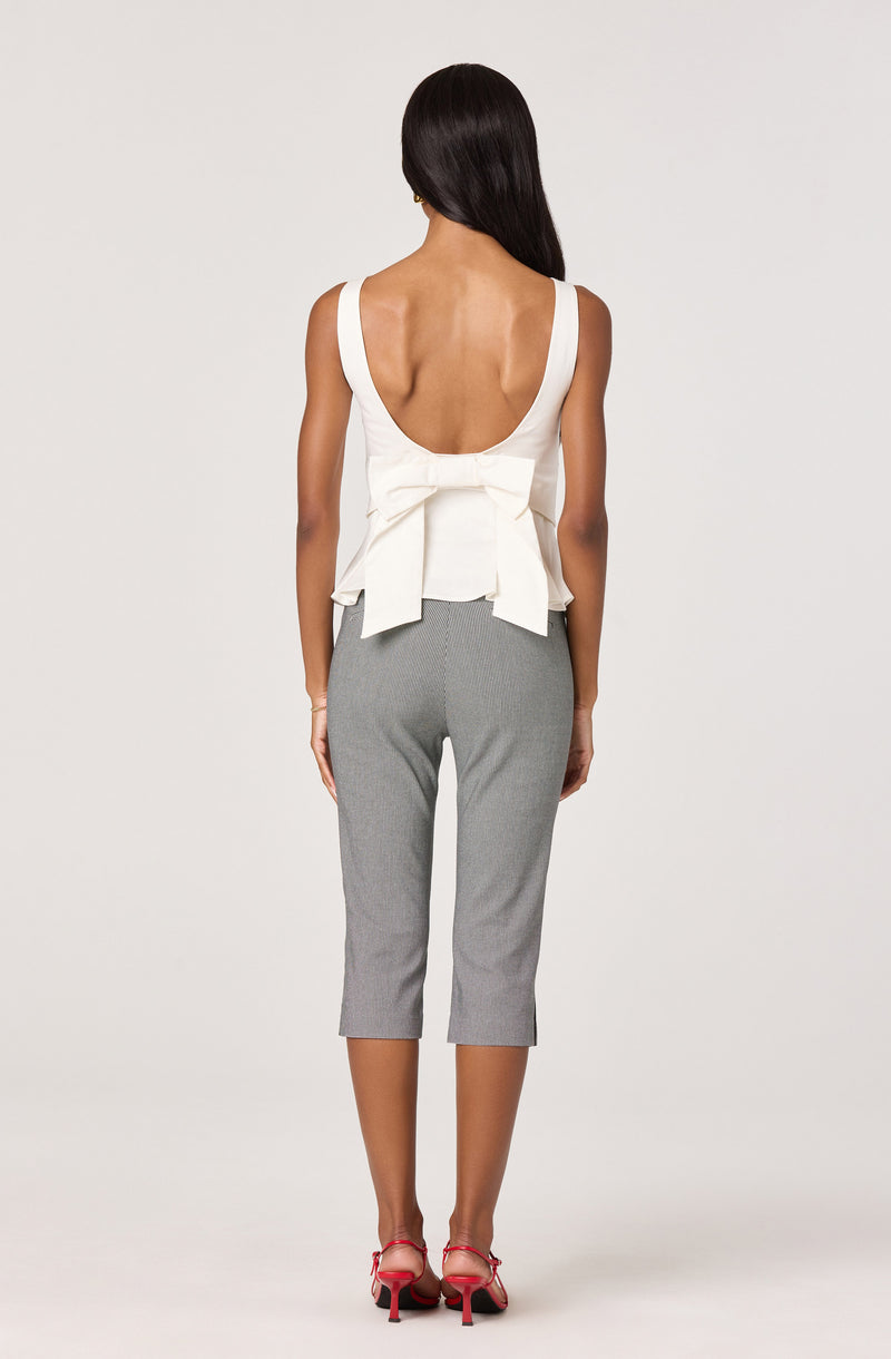 Woman in white sleeveless top with a large bow, gray cropped pants, and red high heels.
