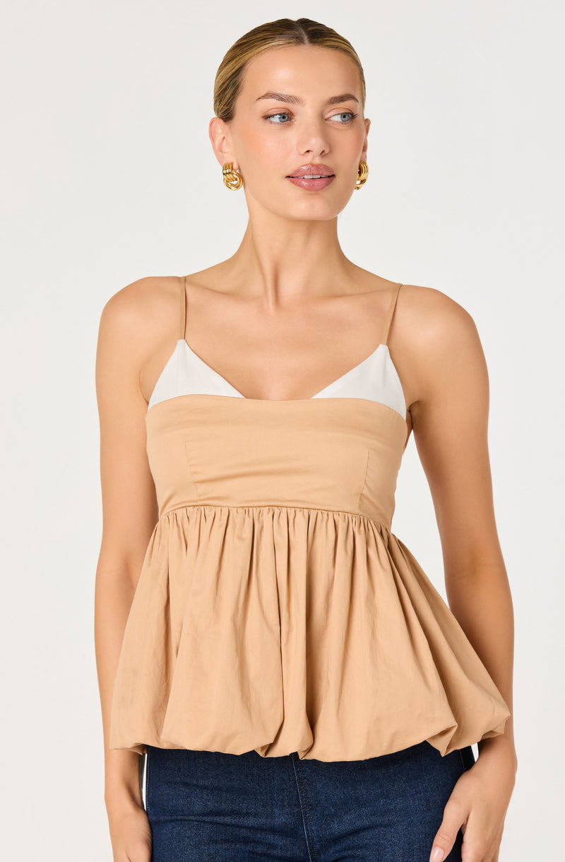 Woman wearing a beige and white sleeveless top with a loose, gathered beige bottom.