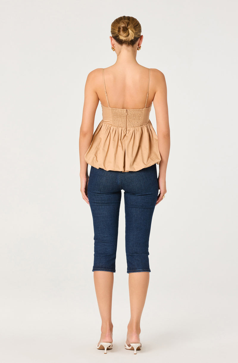 Beige sleeveless top with thin straps and ruching at the back, paired with dark blue capri jeans.