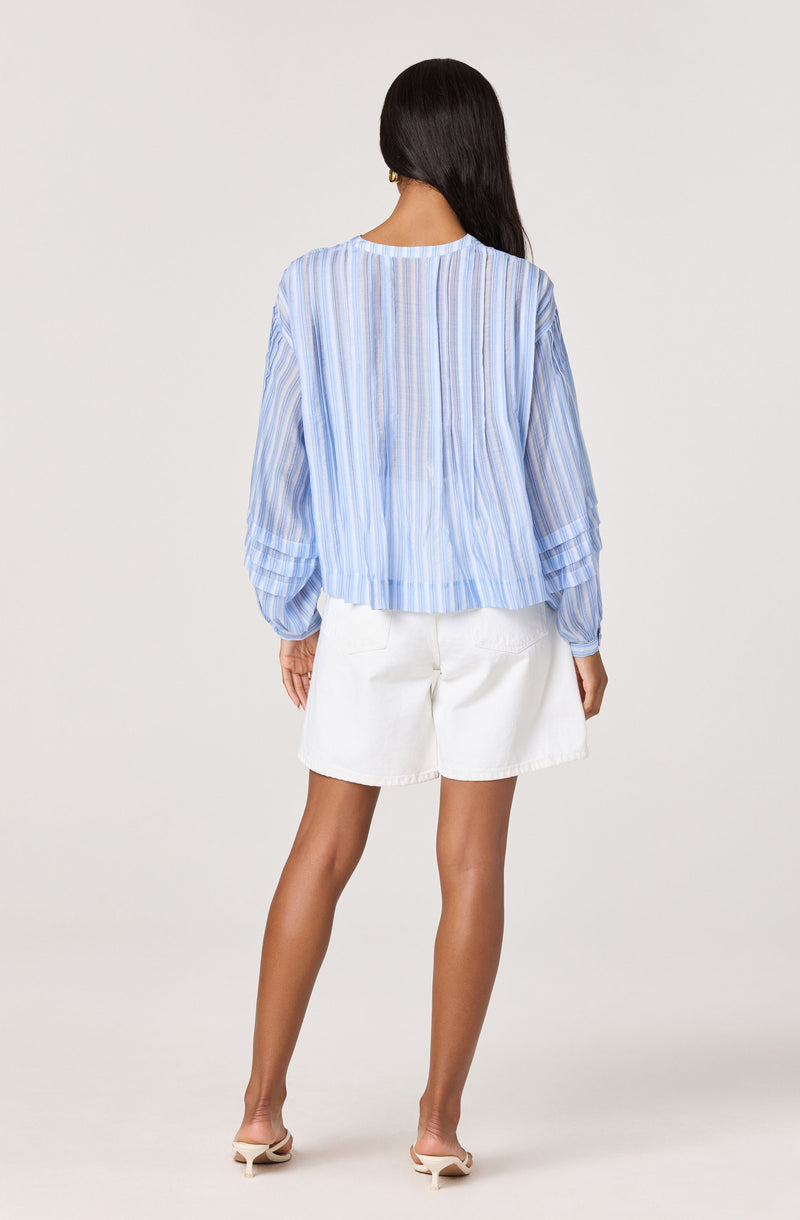 Woman wearing a light blue, striped, long-sleeve blouse and white shorts.