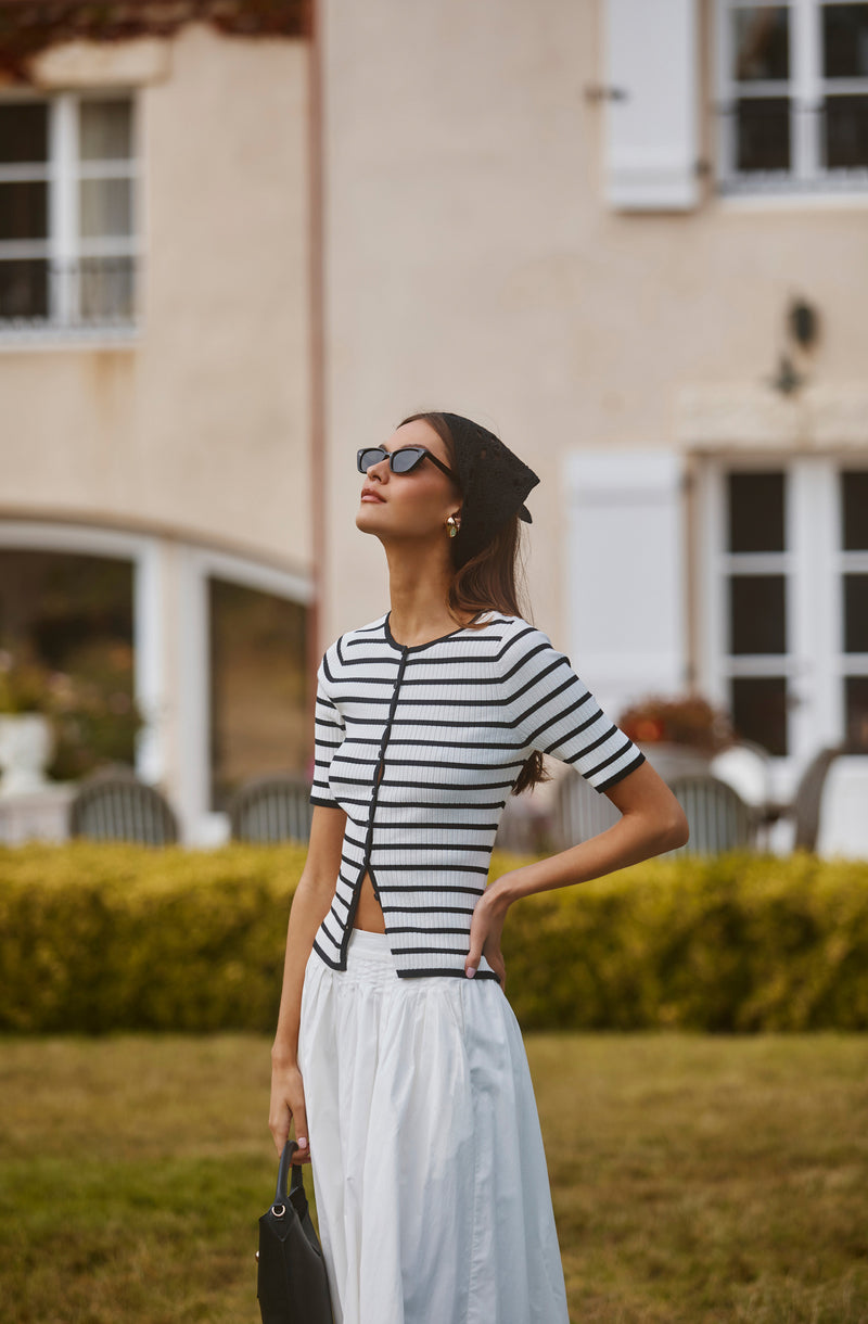 Woman wearing black and white striped short-sleeve top, black headscarf, white skirt, and sunglasses.