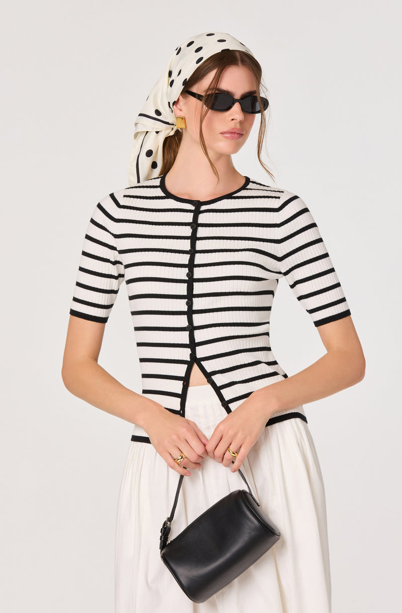 Woman wearing a black and white striped short-sleeve top, white skirt, black sunglasses, and a polka dot headscarf.