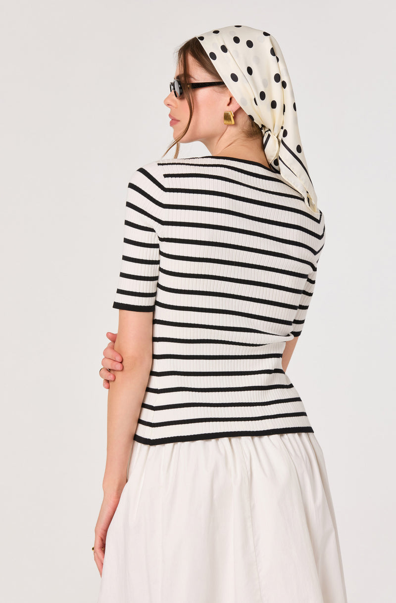 Woman in black and white striped top, white skirt, polka dot headscarf, and glasses.