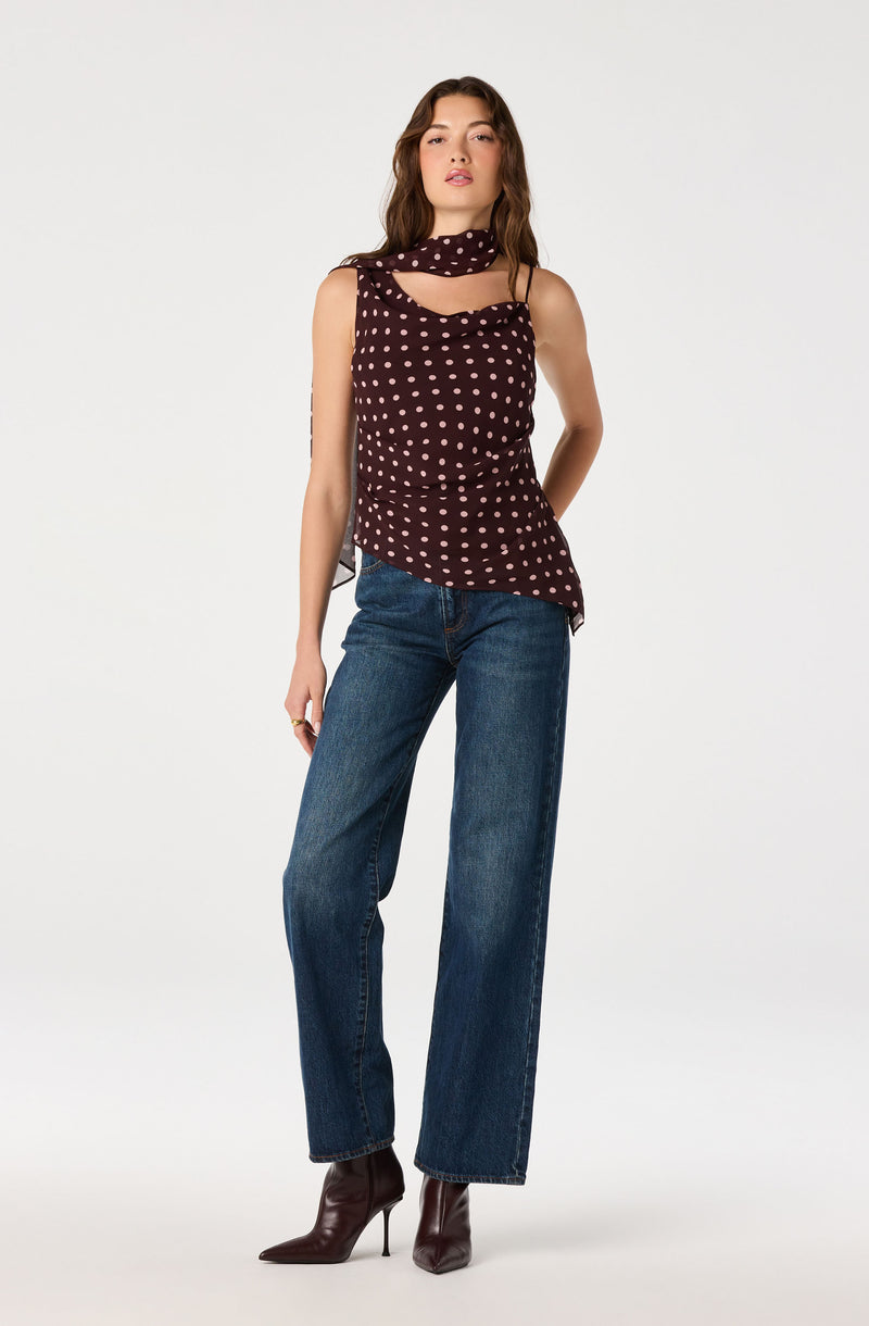 Woman wearing a sleeveless burgundy top with white polka dots, paired with wide-leg jeans and dark ankle boots.