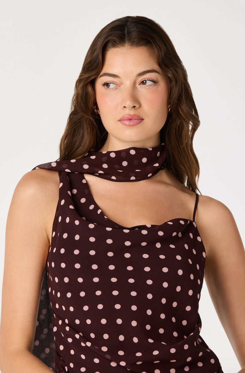 Woman wearing a dark dress with pink polka dots and a matching polka-dot scarf around her neck.