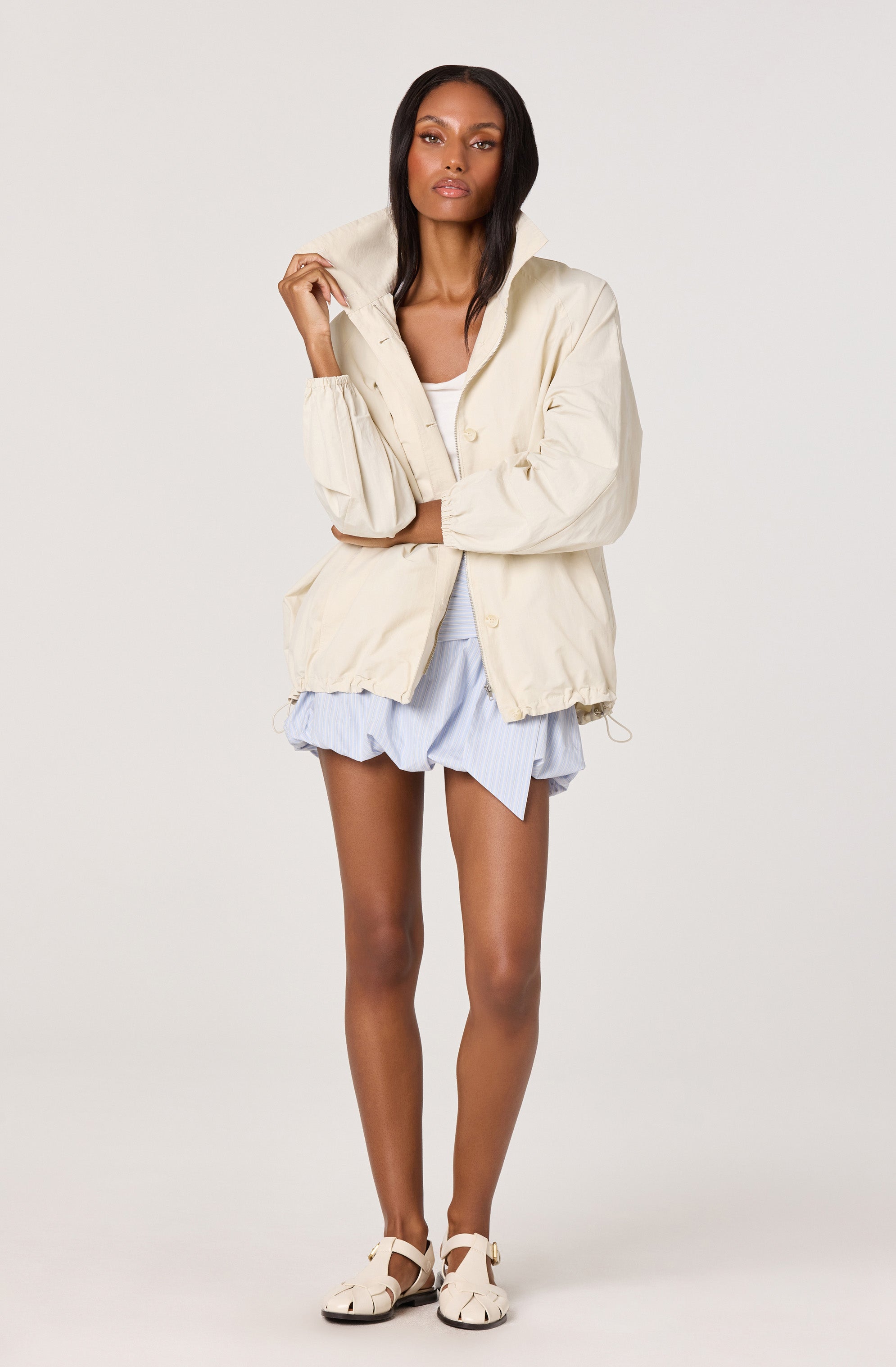 Woman in cream jacket, light blue shorts, and beige shoes.