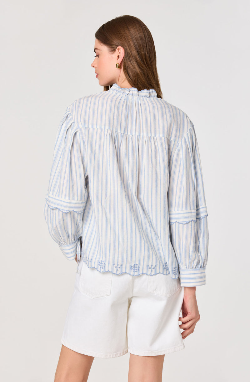 Woman wearing a loose, long-sleeve, striped blouse with ruffled collar and cuffs, white shorts.